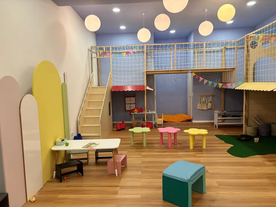 Completed indoor wooden play structure with loft stairs and small colorful tables