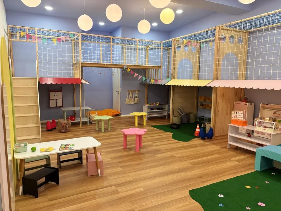 Indoor wooden play structure with bridge, safety netting, and play market stalls