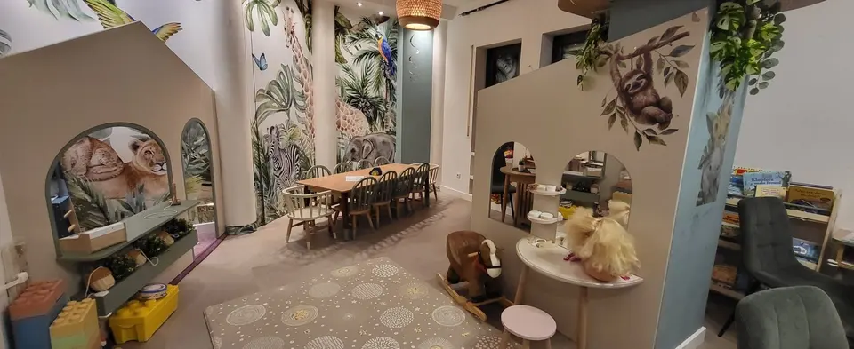 Indoor playroom with custom wooden play structures and jungle wall murals