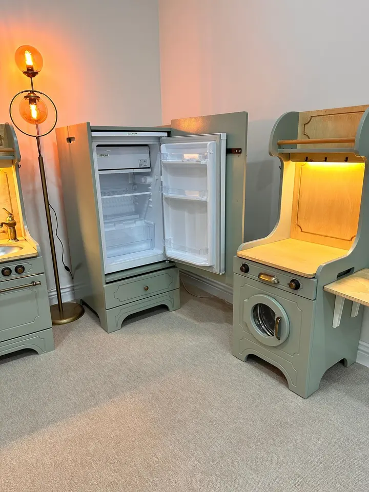 Sage green play kitchen setup with washing machine and built-in refrigerator