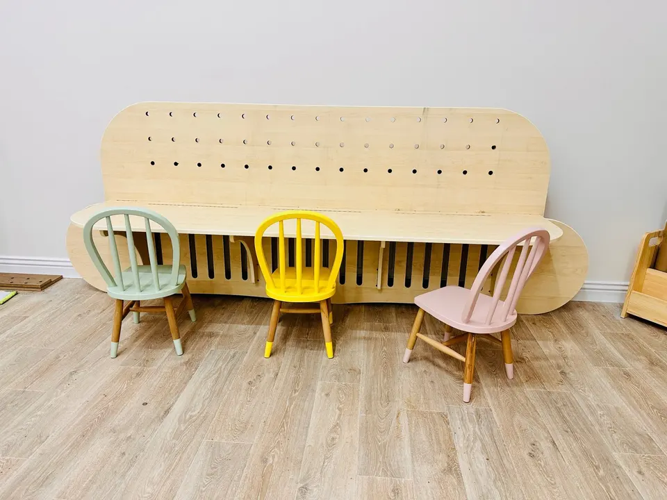 Curved wooden children activity table with pastel chairs in a playroom
