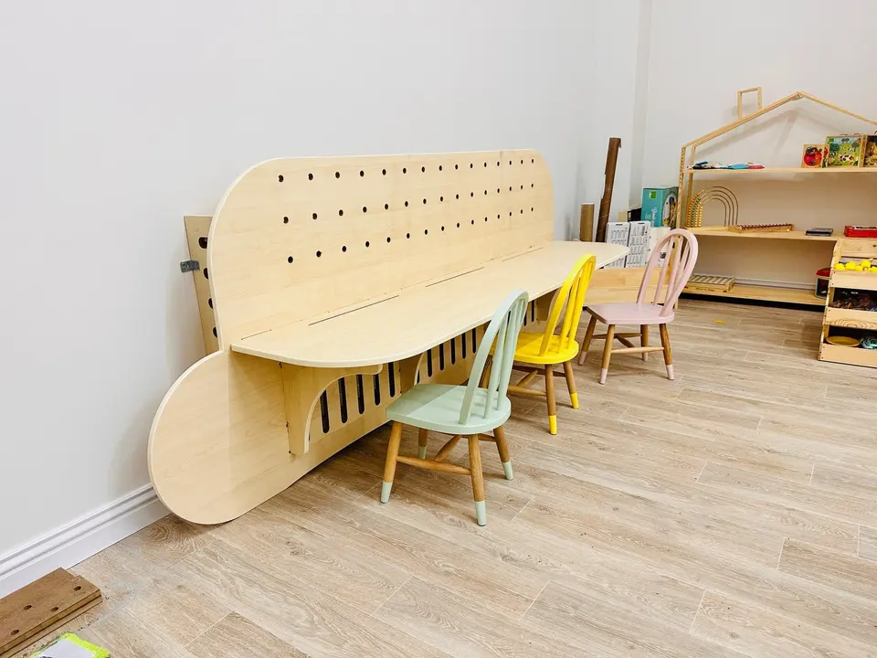 Long natural wood sensory activity table with colorful chairs in playroom