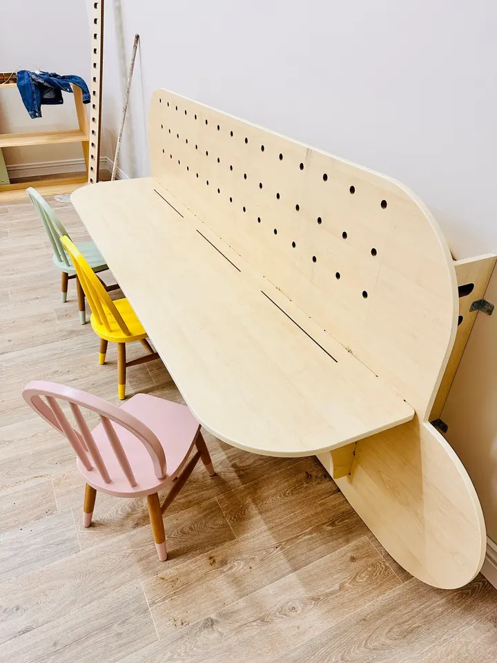 Angled view of foldable wooden study desk with pegboard and chairs