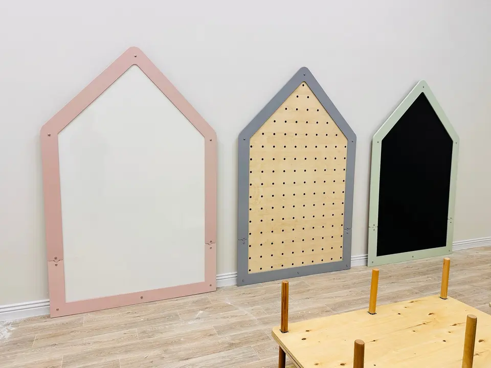 Three house-shaped wall activity boards including whiteboard, pegboard, and chalkboard