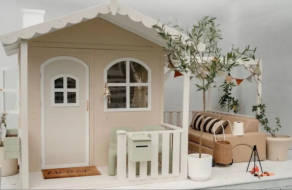 Beige wooden playhouse with front porch, lounge bench, and potted plants
