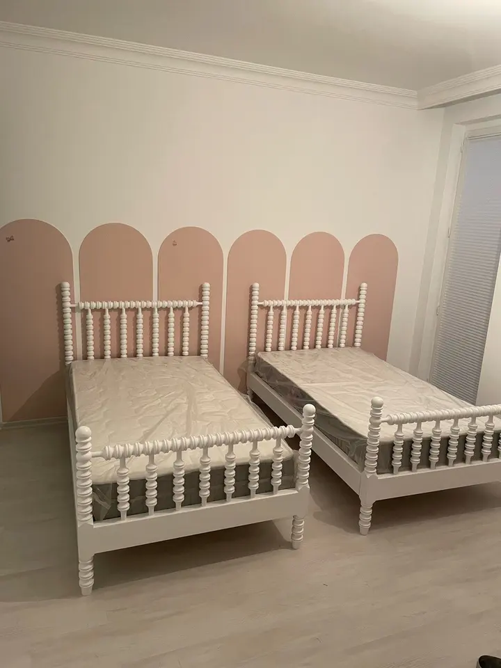 Pair of white spindle beds against arched wall painting in kids bedroom