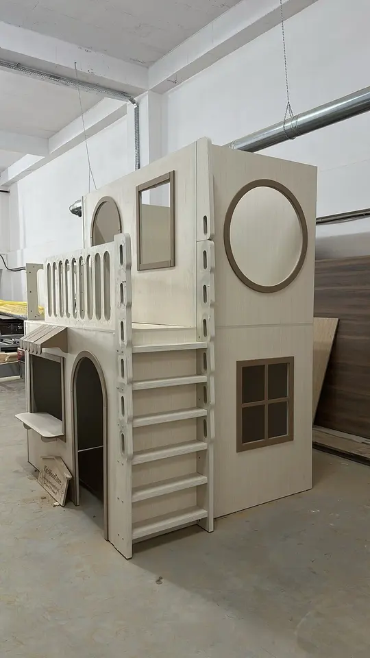 Finished two-story wooden playhouse with upper balcony and ladder in workshop
