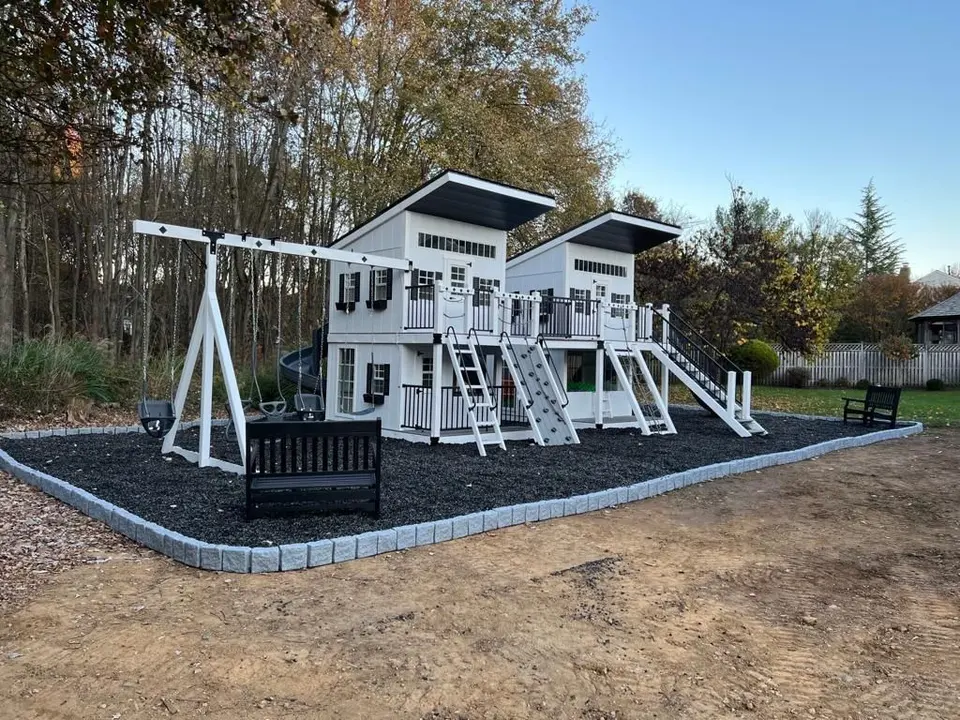 Large outdoor wooden playhouse structure with slide, swings, and climbing wall