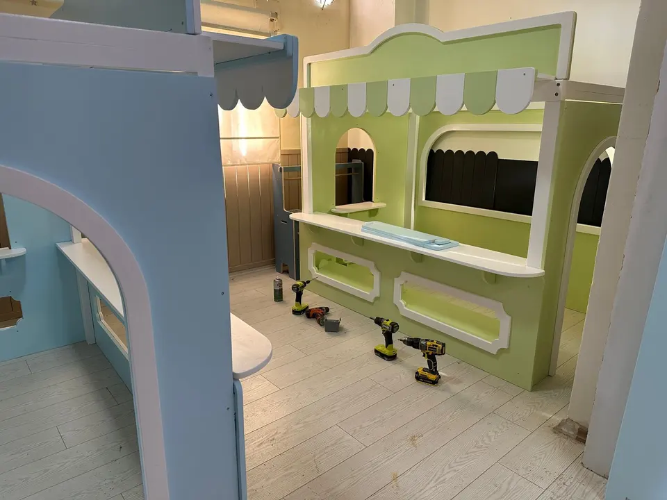 Green wooden play market stall with tools on floor during indoor installation