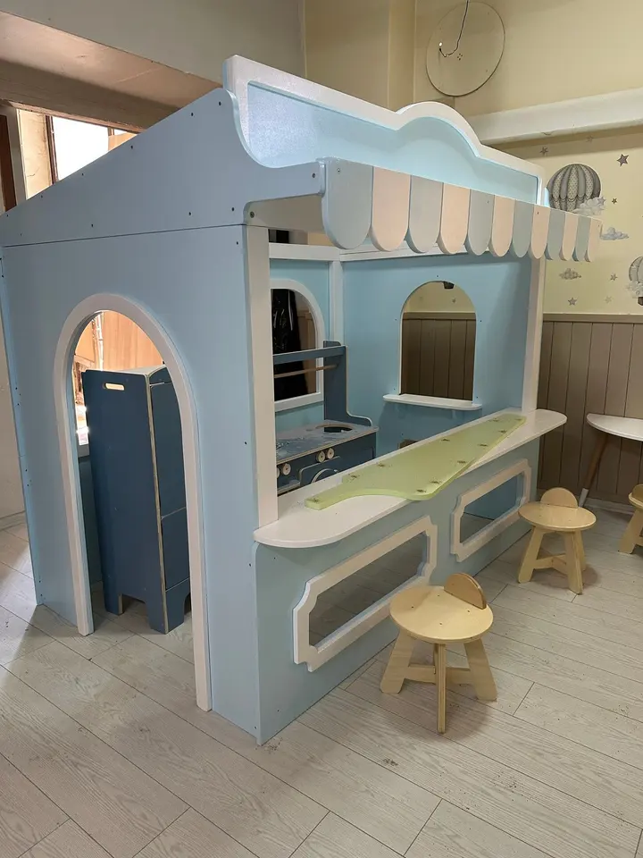 Light blue wooden playhouse stall with striped awning and stools inside playroom