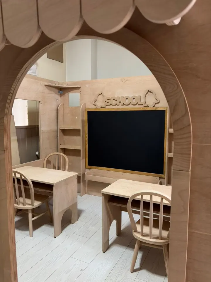 View through doorway into a wooden play schoolroom with desks and chalkboard
