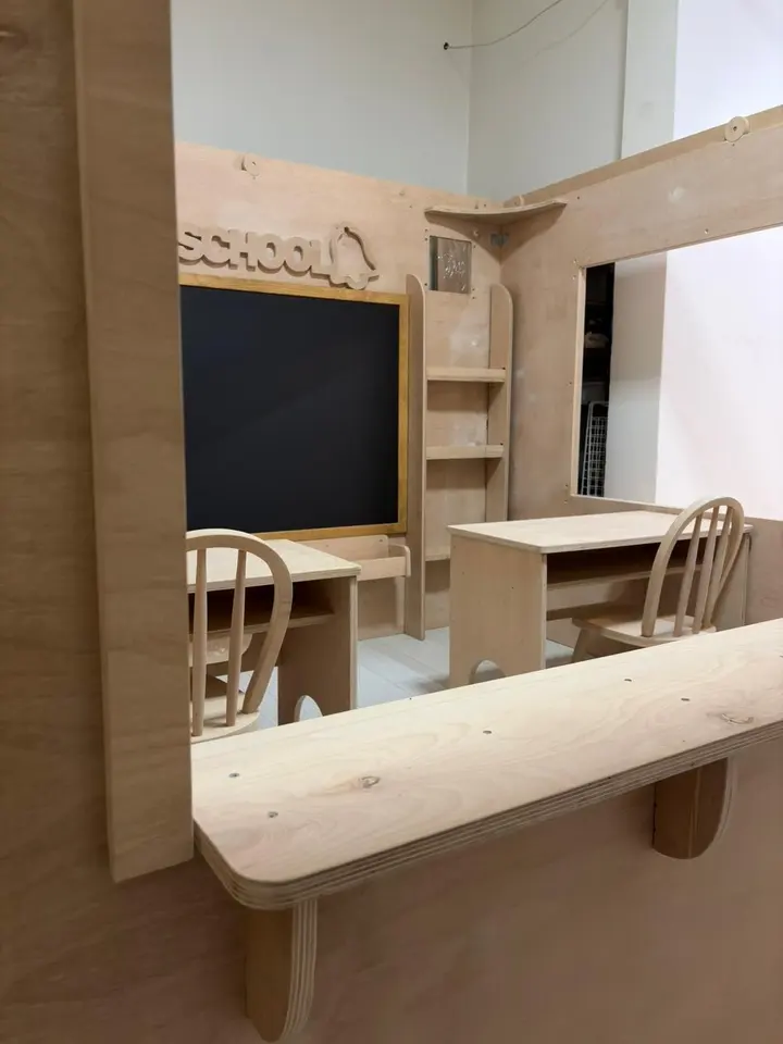 Side window counter view into wooden classroom playhouse with desks and chalkboard