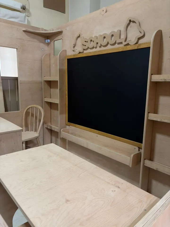 Wooden desk foreground view inside school playhouse with wall-mounted chalkboard