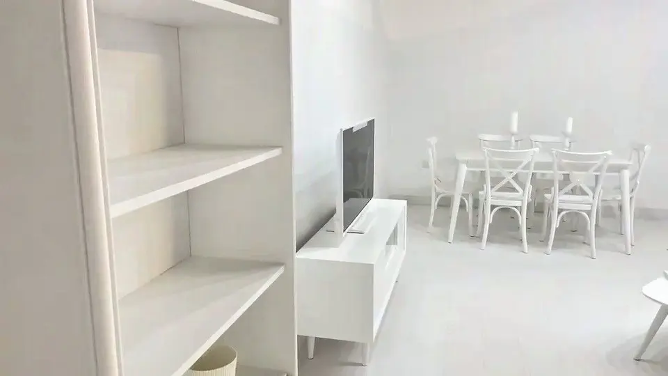 All-white living room set with dining table, chairs, shelving unit, and TV console