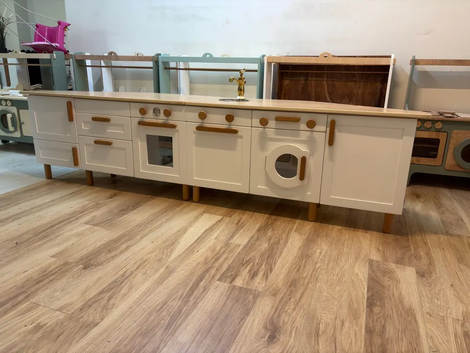 Modular white play kitchen cabinet with sink and appliances on wooden floor