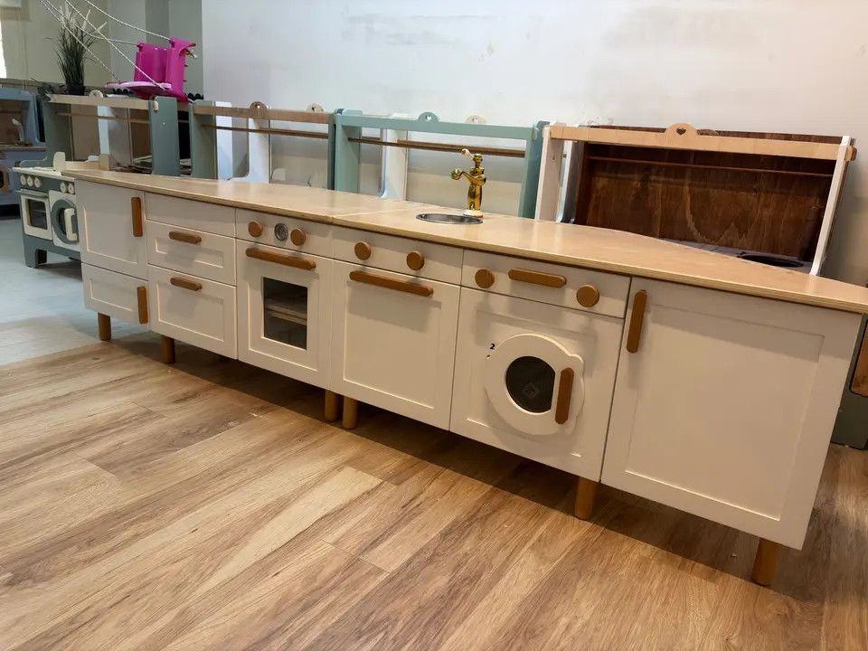 Long white wooden play kitchen counter with washing machine and oven
