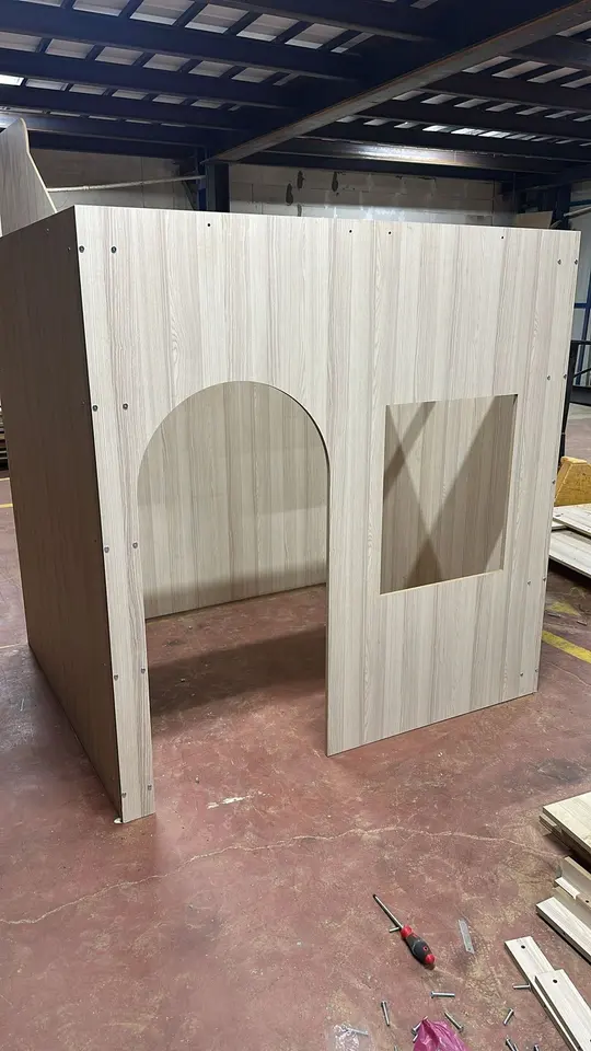 Wooden playhouse under assembly on workshop floor with tools and cutouts