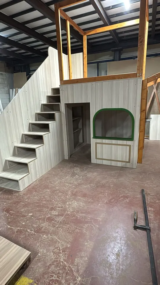 Wooden playhouse with stairs and open play platform in a workshop