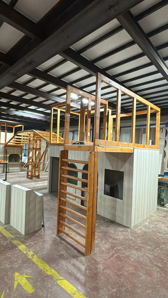 Wooden play structure with ladder and elevated platform under construction in workshop