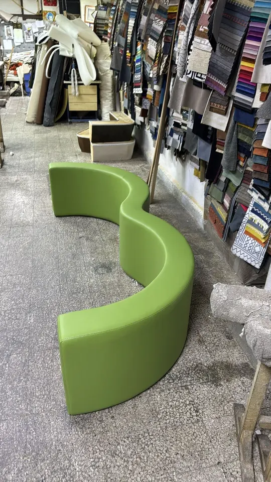 Curved green modular padded bench assembled on upholstery workshop floor