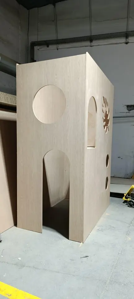 Unfinished wooden play tower structure with circular cutouts in workshop