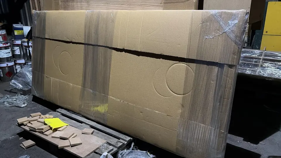 Large wooden panel wrapped in cardboard and plastic stretch wrap