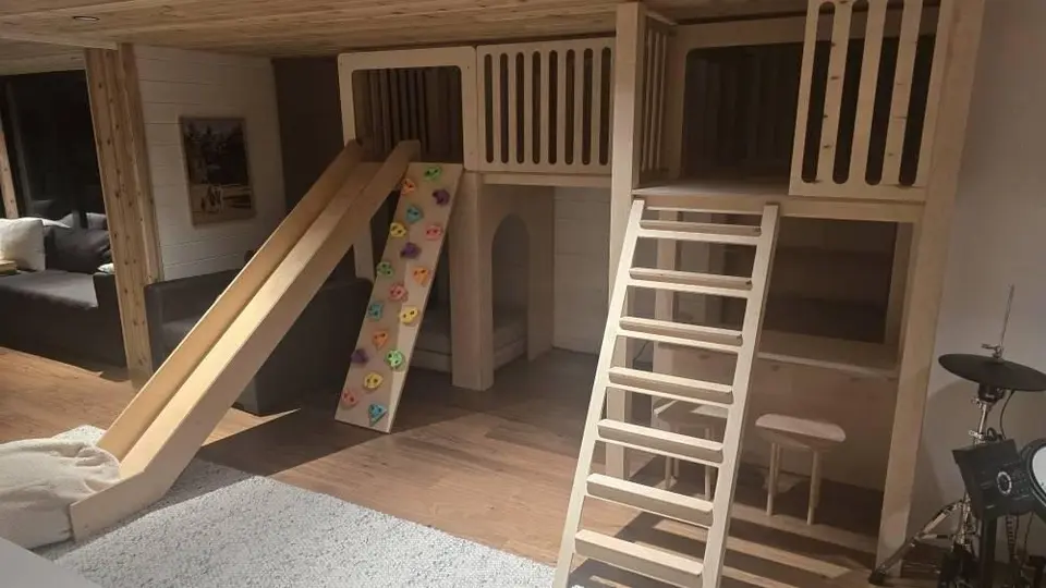 Custom wooden loft playhouse with slide, ladder, and climbing ramp installed indoors
