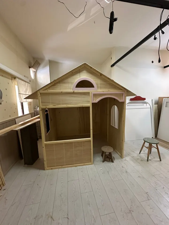 Unfinished wooden playhouse assembled on workshop floor with stools