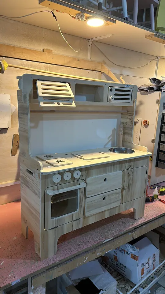Finished natural wood play kitchen unit in a carpentry workshop