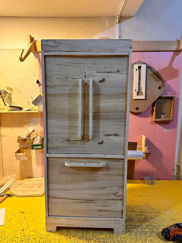 Handcrafted wooden toy refrigerator standing on a workshop table