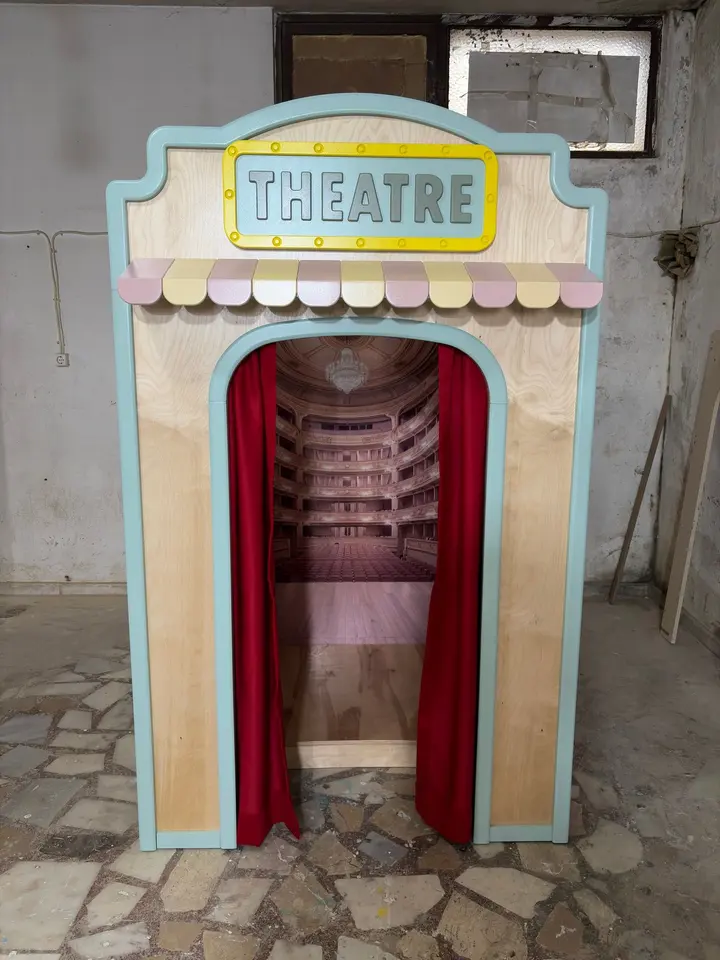 Wooden theatre playhouse with red curtains and printed backdrop in workshop