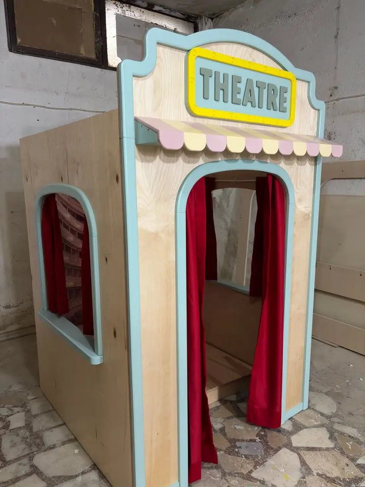 Three-quarter view of wooden theatre playhouse with striped awning in workshop